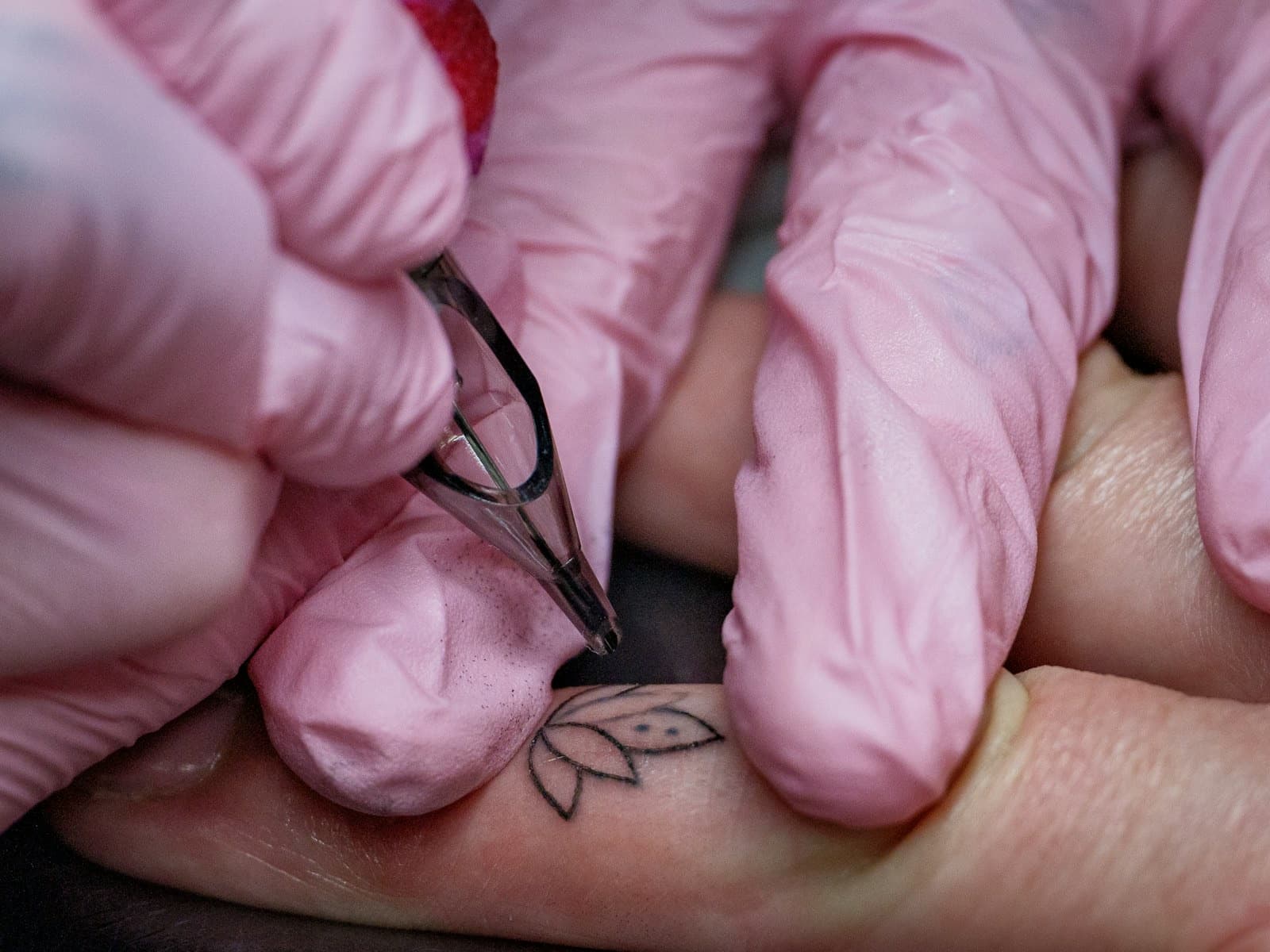 Tatuadora a tatuar uma pequena flor num dedo